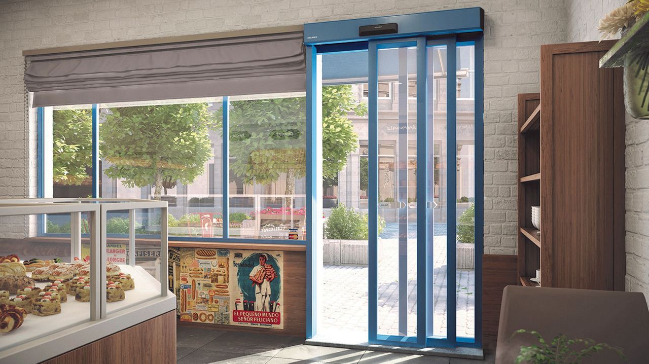 Una farmacia y tienda de pequeño tamaño con una puerta deslizante de vidrio azul. Una mesa con una taza de café y una planta. 