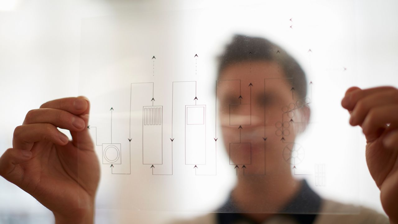 A man is holding up a transparent foil of a electric circuit. The print is the only thing in focus