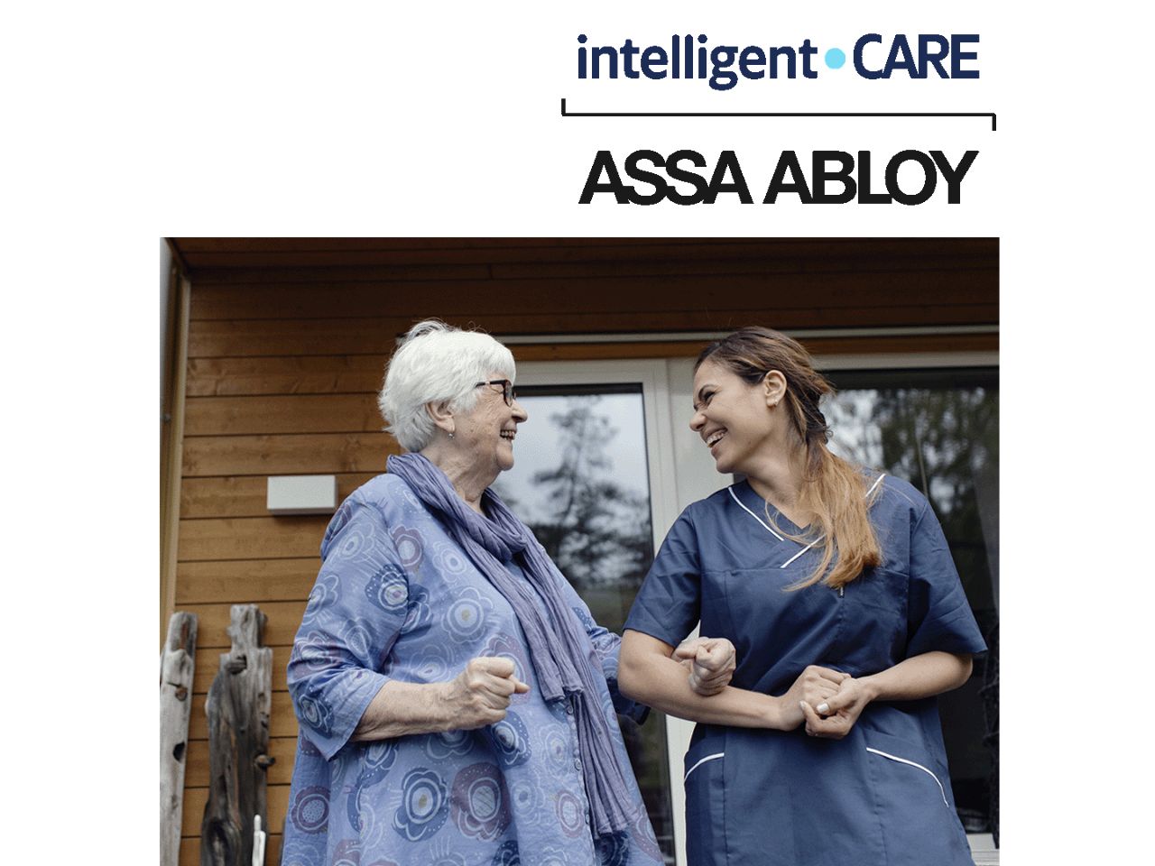 Senior woman standing outside the entrance door with a younger woman in nurse clothes. Inteligent Care logotype above.