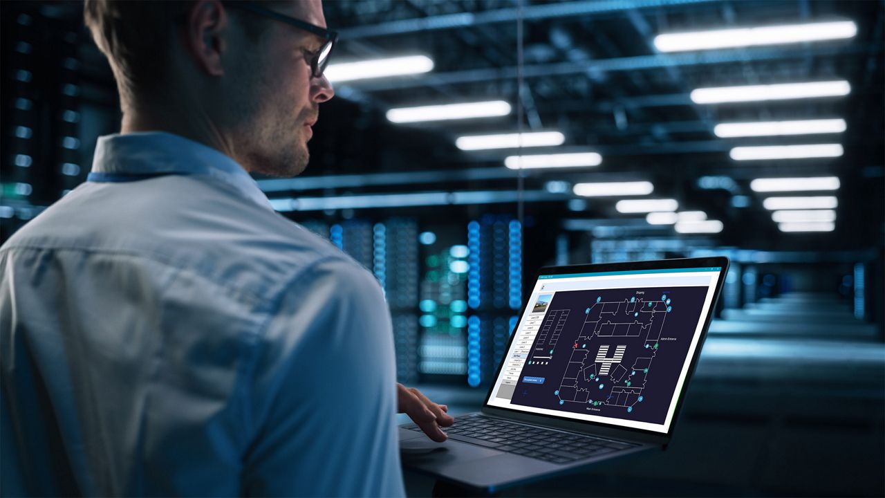 Security manager is looking at the laptop screen, while checking the floorplan of the building.