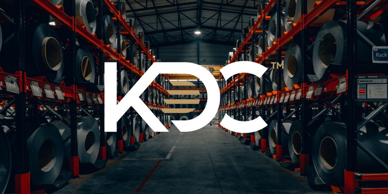View of the KDC industrial warehouse showcasing metal coils in a variety of colors, arranged around the KDC logo positioned at the center.