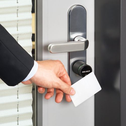 Hand holding an access card up to an Aperio wireless lock cylinder on a glass office door
