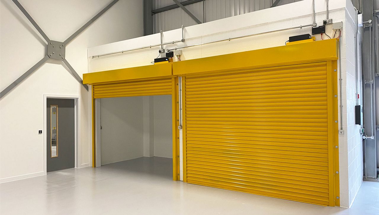 Image: Two yellow painted ASSA ABLOY fire roller shutter in-situ within a manufacturing centre  