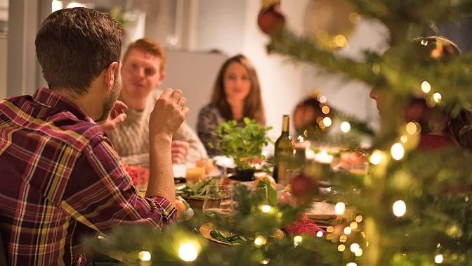 mensen aan een eettafel bij een kerstboom met lichtjes