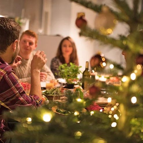 mensen aan een eettafel bij een kerstboom met lichtjes