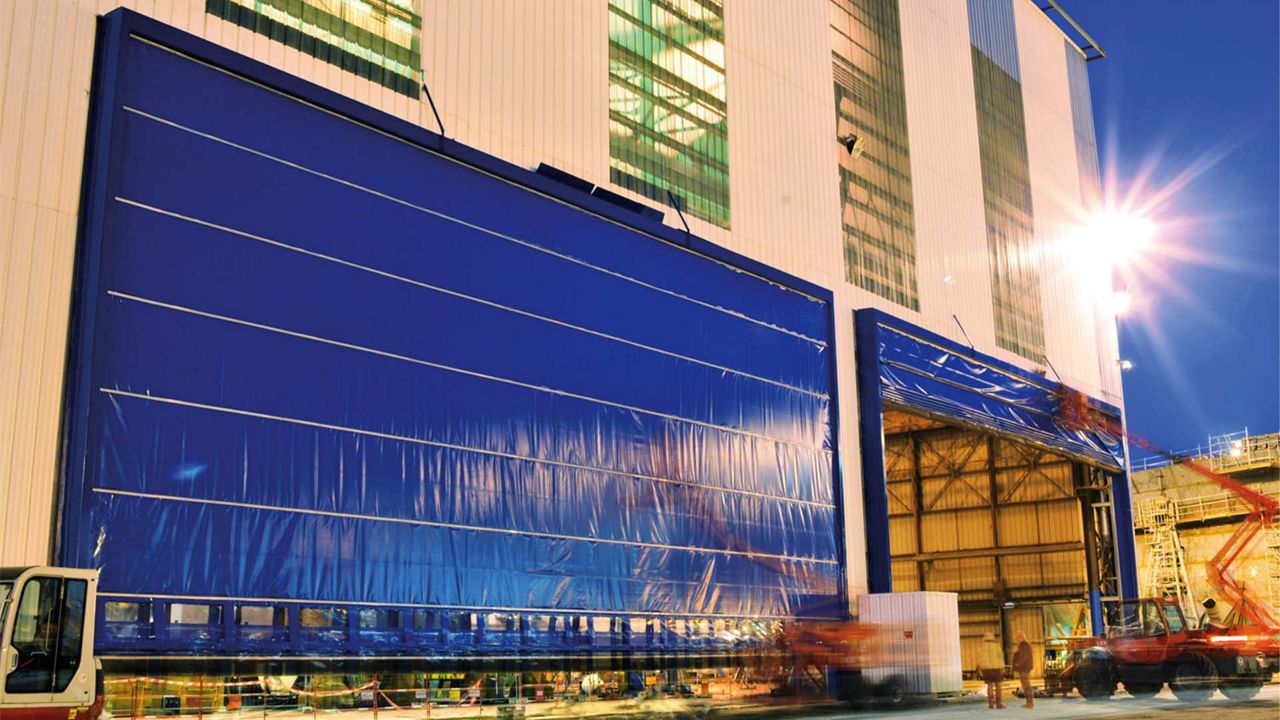  Zwei große blaue Tore an einem weißen Gebäude, eines der Tore wird geschlossen. 