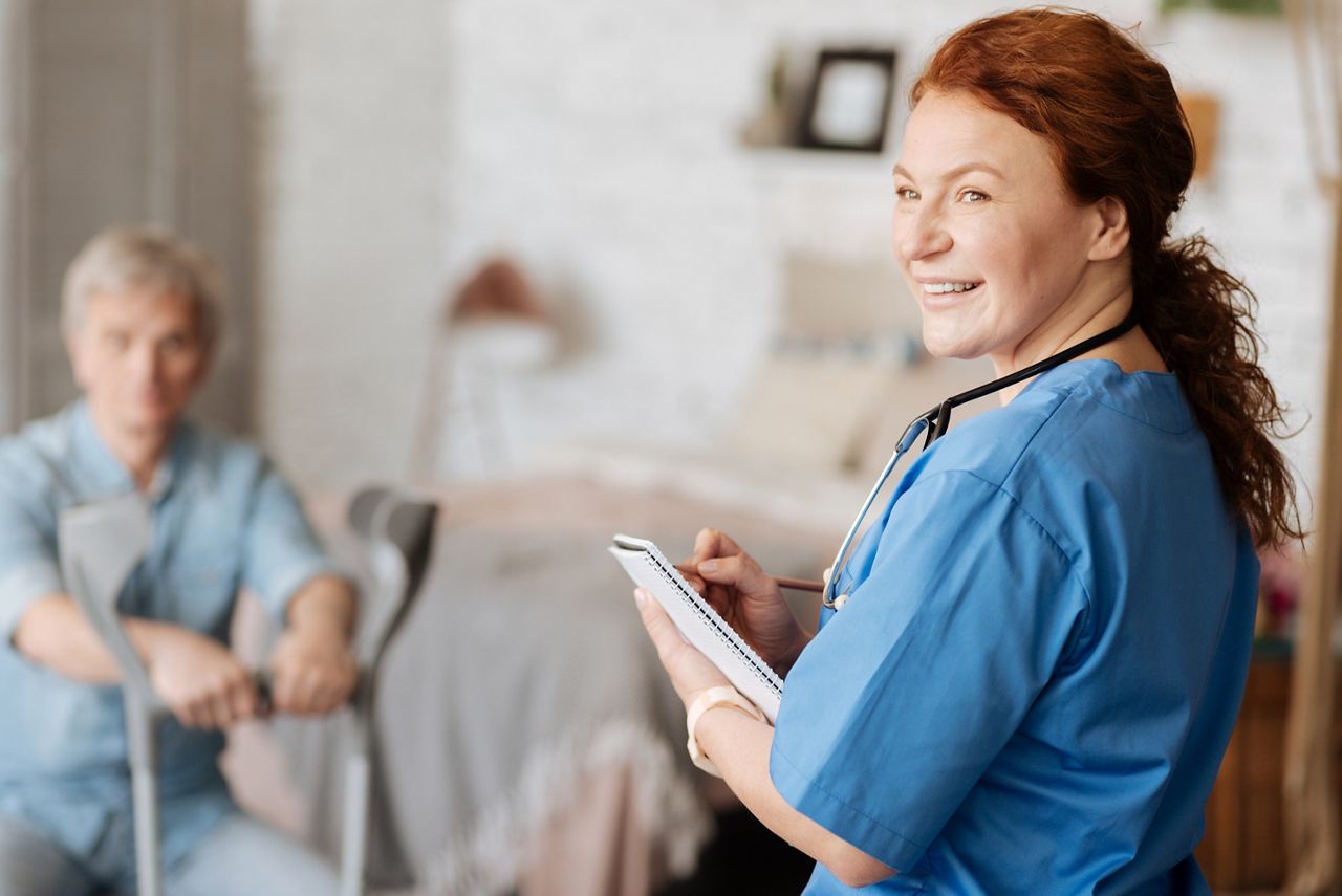 Female nurse looking at someone while helping a man with crutches.