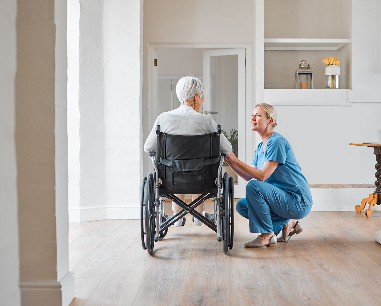 Nurse kneeling besides a woman in a wheelchair with her back to the camera.