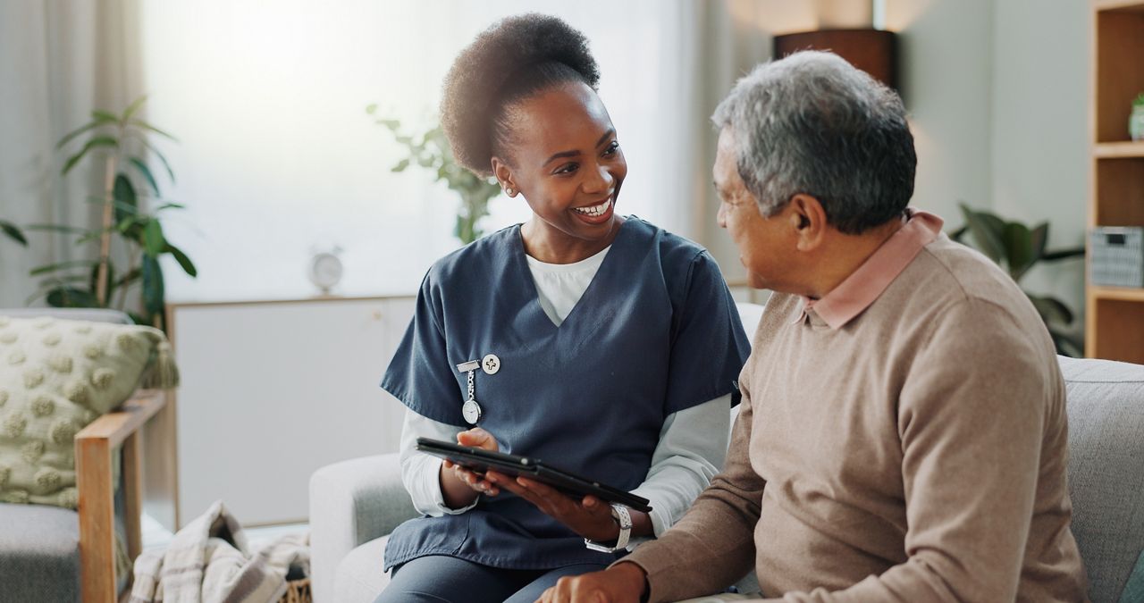 Nurse and senior man sitting in a sofa while looking at something on a tablet.