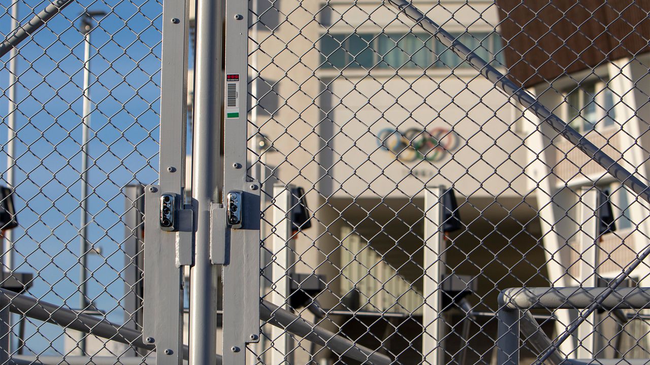 A locked fence outside the stadium, with Olympic rings visible on the wall behind the fence.