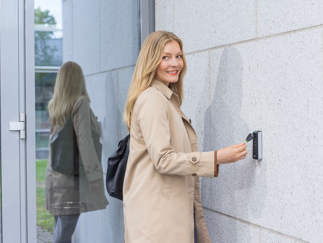 Une femme approche une clé électronique d'un lecteur mural fixé à côté d'une porte vitrée