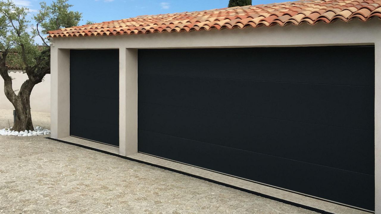 Porte de garage résidentielle à panneaux horizontaux noirs installée en façade d'un garage, modèle DUO TRACTION.