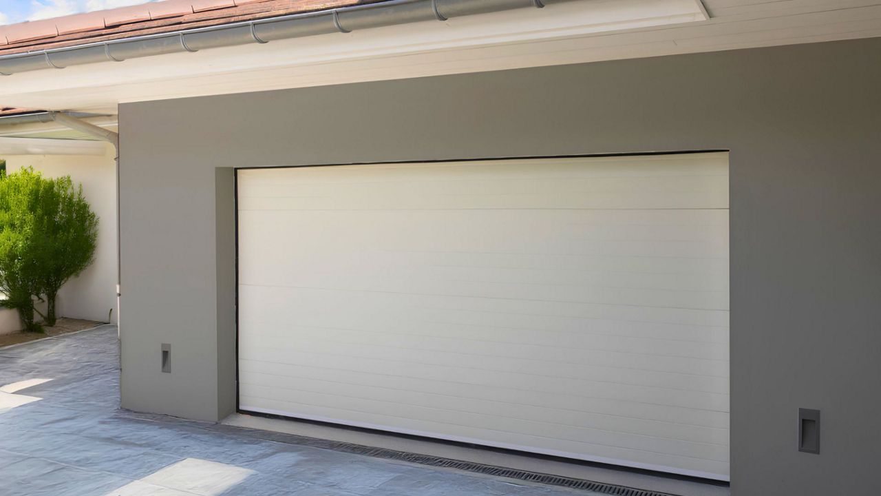 Maison beige vue de face avec un garage fermé par une porte grise foncée.