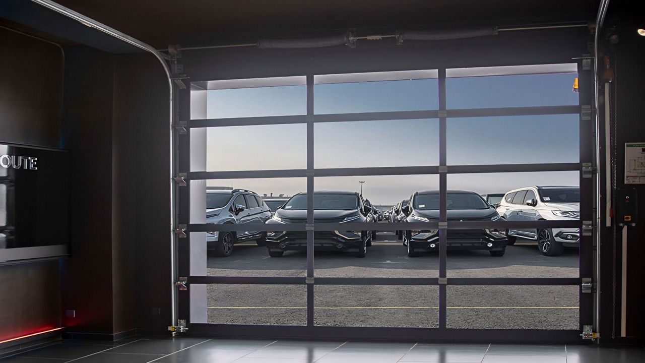 Porte sectionnelle industrielle entièrement vitrée offrant une vue sur un parking automobile depuis l’intérieur d’un bâtiment.