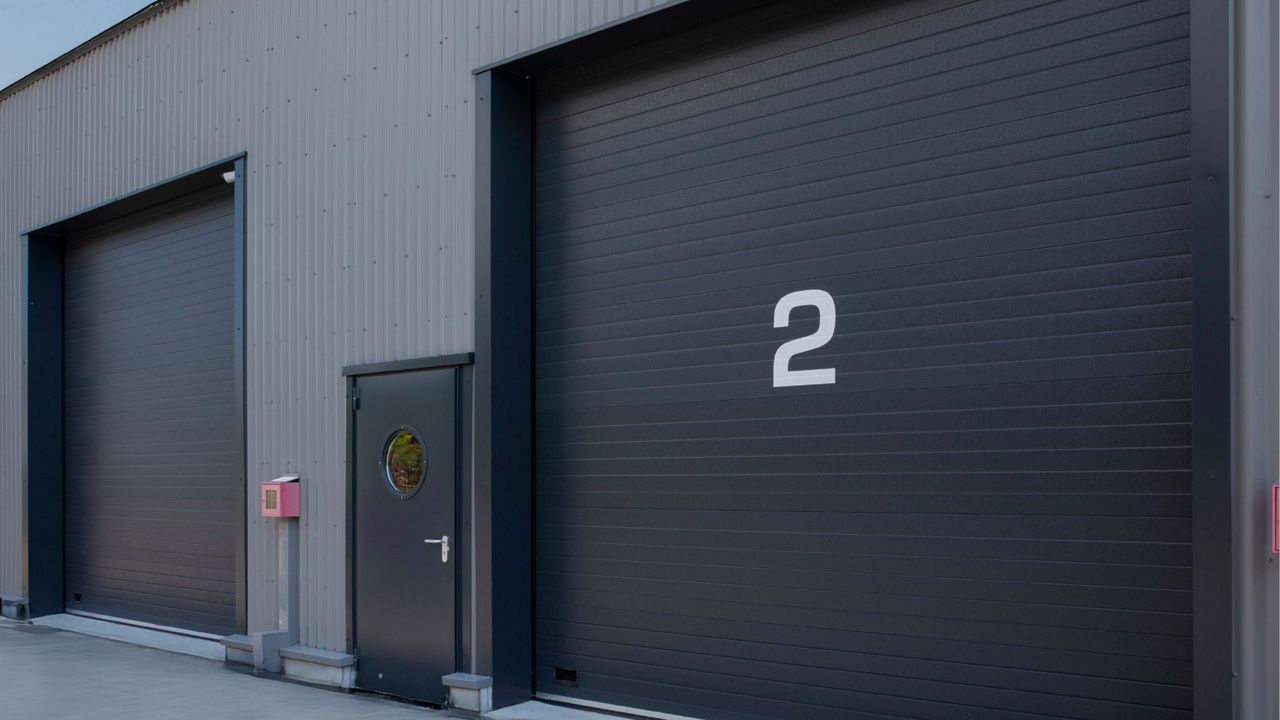 Porte sectionnelle industrielle isolée noire installée en façade d’un bâtiment industriel avec numéro de quai.