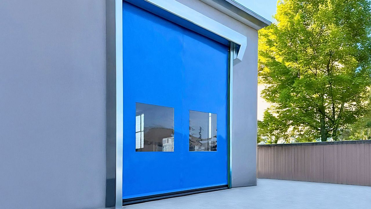 Porte souple rapide à enroulement auto-réparable bleue avec hublots intégrés, installée sur un bâtiment industriel.