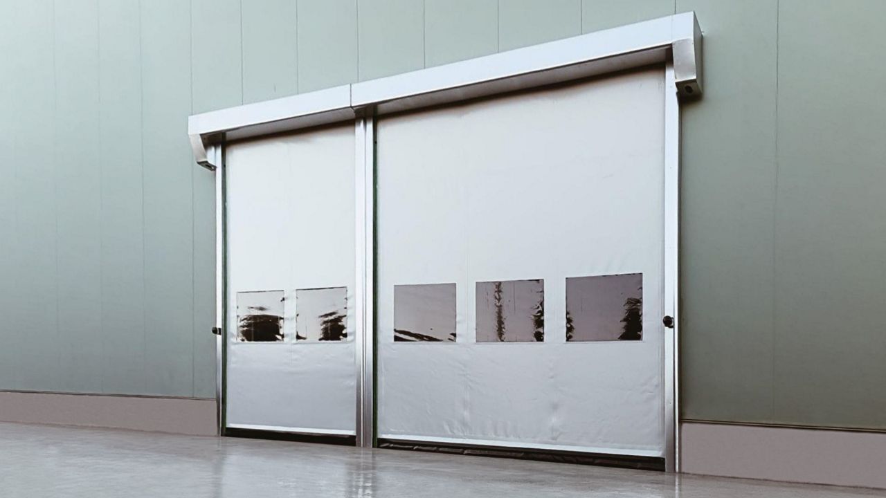 Porte souple rapide à enroulement auto-réparable blanche, avec hublots transparents, installée sur un bâtiment industriel.