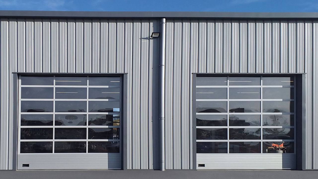Portes sectionnelles industrielles avec vitrage panoramique installées en façade d’un bâtiment industriel.