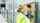 Un technicien spécialisé dans les équipements de sécurité (casque, lunettes, gilet fluorescent) inspecte une porte sectionnelle dans un bâtiment industriel et actionne le boîtier de commande afin d'analyser un dysfonctionnement.
