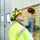 Un technicien spécialisé dans les équipements de sécurité (casque, lunettes, gilet fluorescent) inspecte une porte sectionnelle dans un bâtiment industriel et actionne le boîtier de commande afin d'analyser un dysfonctionnement.
