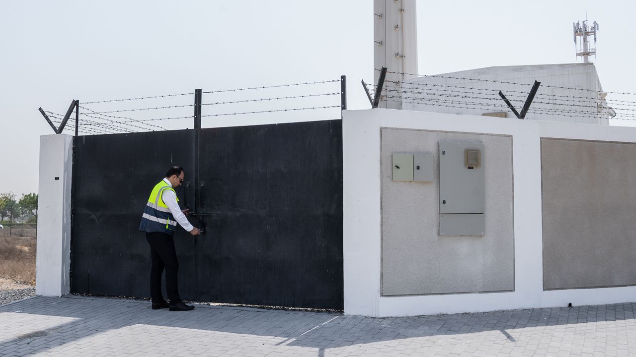 Persoana de securitate deschide o poartă metalică neagră.