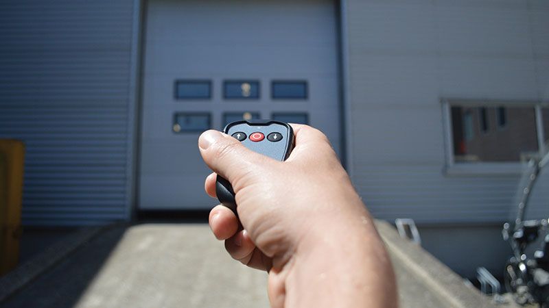 Technicien ASSA ABLOY programmant un émetteur original pour une porte sectionnelle industrielle
