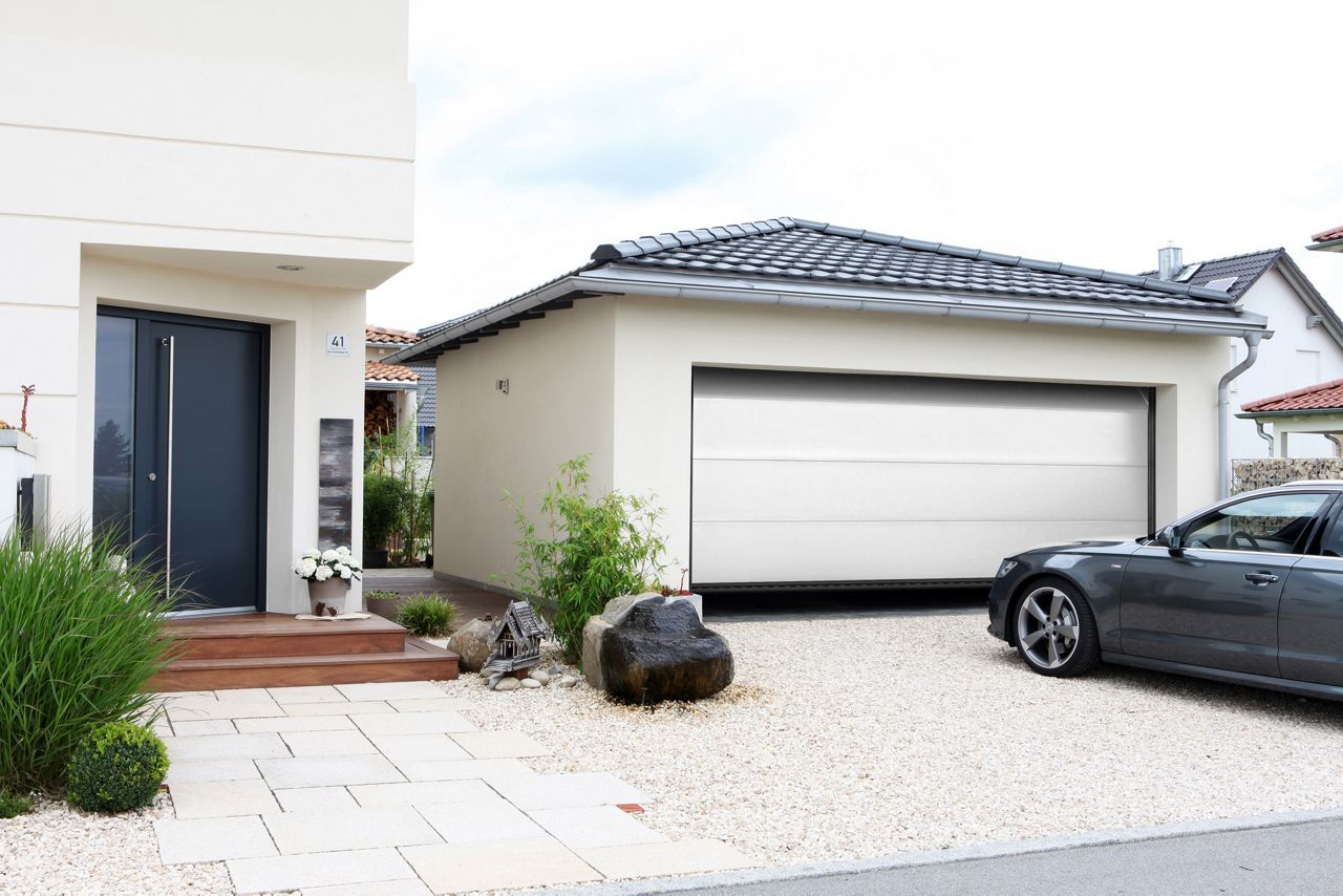 Maison beige vue de face avec un garage fermé par une porte grise foncée.