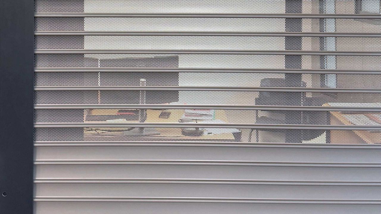 Rideau métallique simple paroi modèle P57 avec lames micro-perforées avec visibilité sur un bureau.