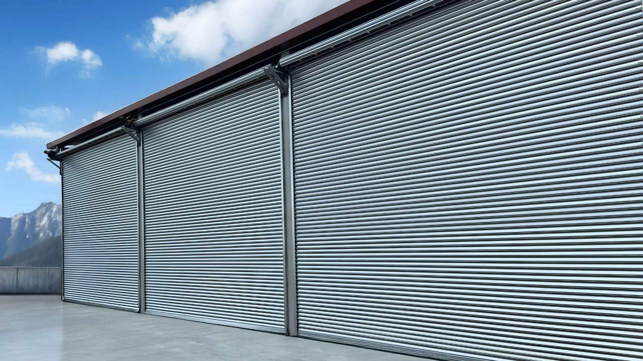 Rideaux métalliques simple paroi modèle P97 avec lames bombées, installés en façade d’un entrepot avec grandes ouvertures.