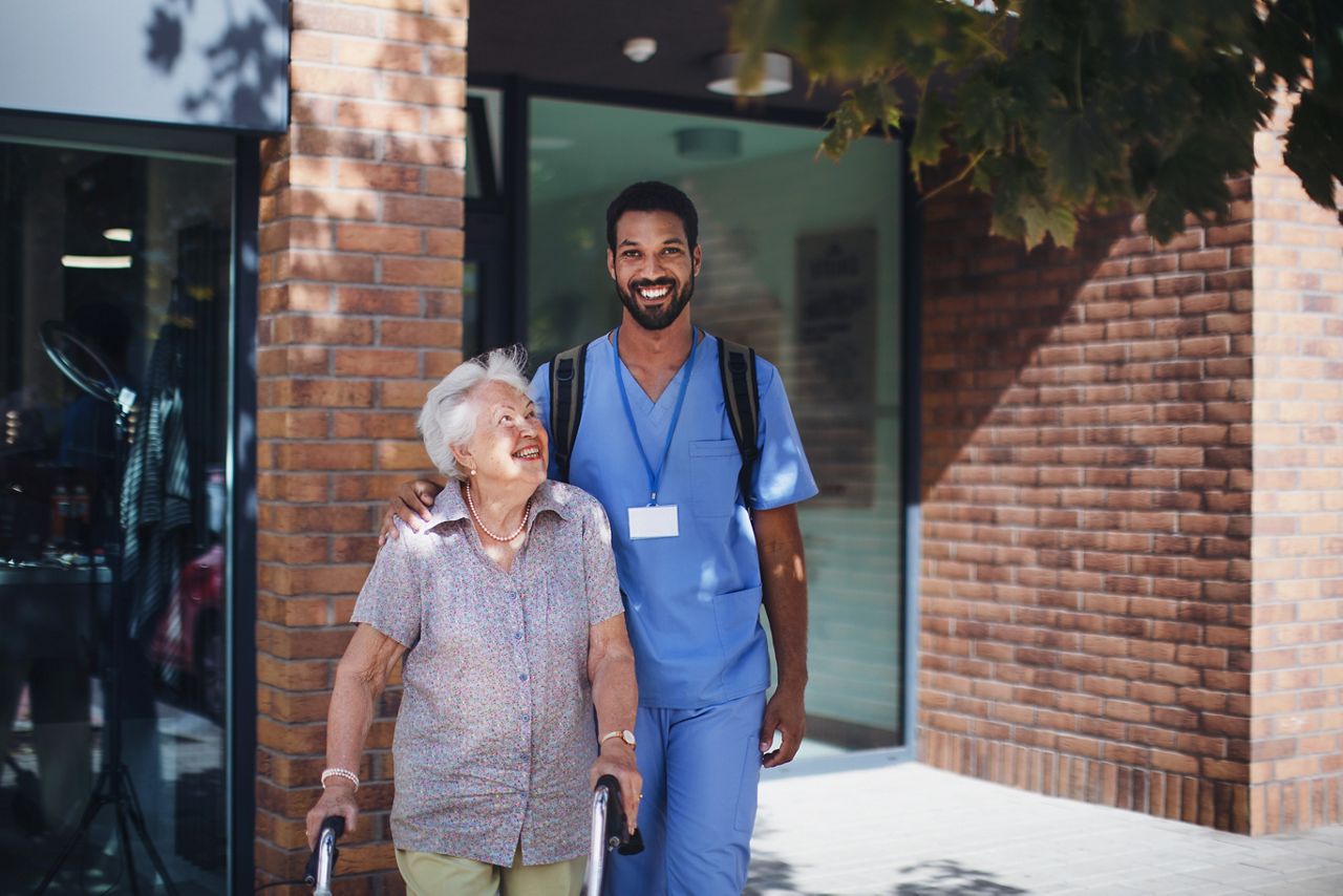 Senior woman and male nurse walking out into the sunshine.