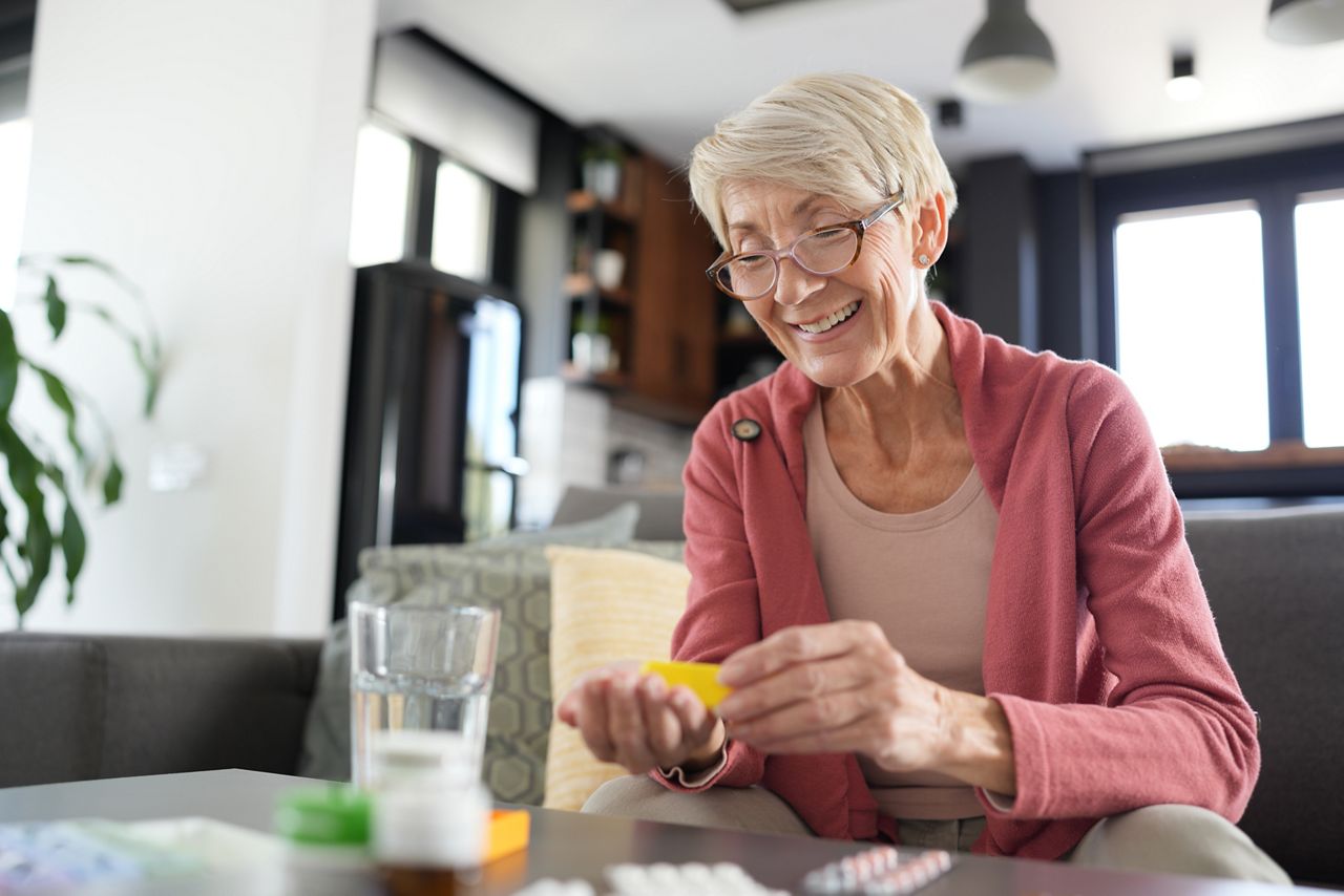 Senior woman sorting out her medication sitting in a sofa.
