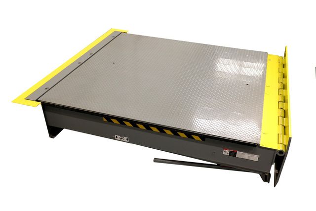 Image: Angled view of a gray Serco dock leveler with a textured steel platform, yellow guard barrier along the edge, and black-and-yellow safety markings on the front.