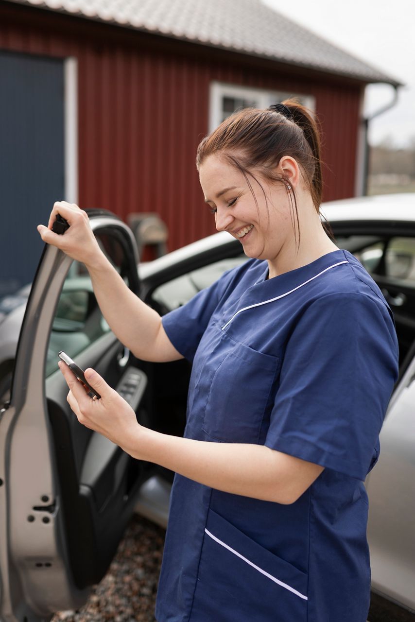 Smiling home care nurse exiting her care smiling while looking at a mobile screen.