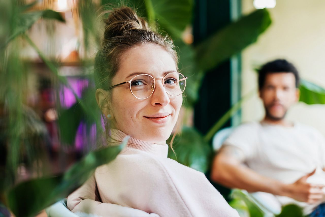 Woman sitting amongst green plant looking right at us.