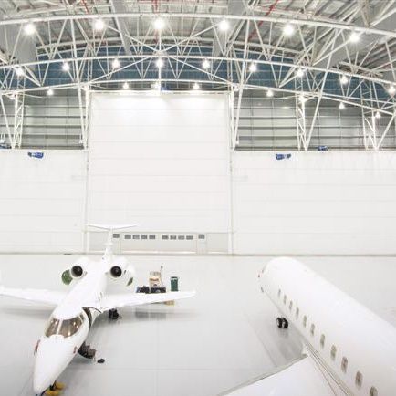 Hangar de aeroporto, com dois aviões brancos e cinco portas para hangares brancas