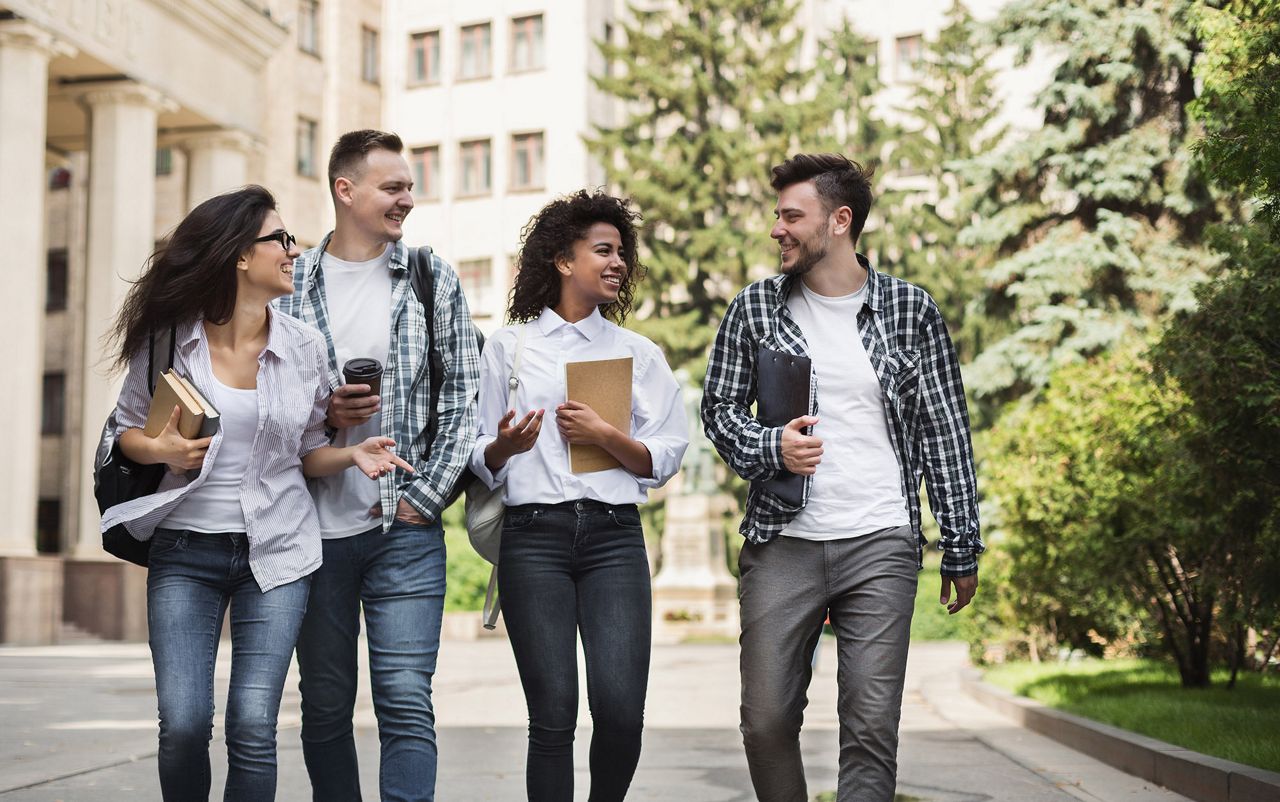 Image of diverse students smiling and walking together on university campus, highlighting campus safety and security.