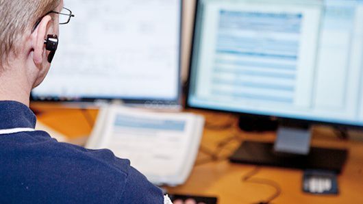 Man sitter vid dator och pratar i telefon.