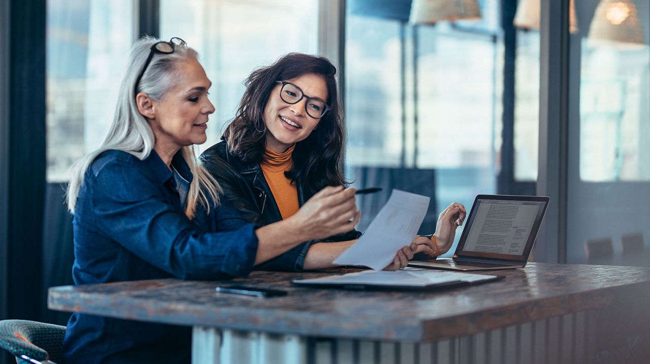 Two smiling women in an office environment looking at a document.