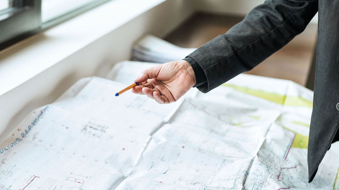 Hand with pencil pointing at a drawing.