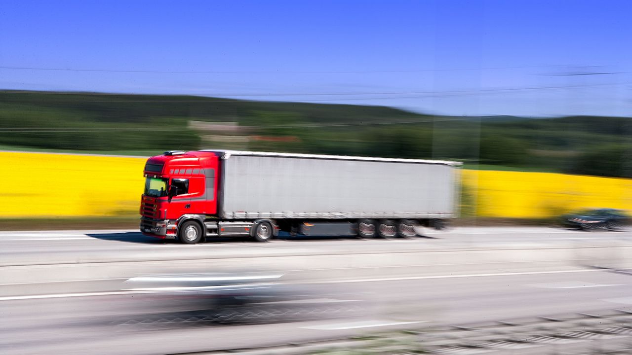 Lastbil med släp på väg genom landskap med gula rapsfält.