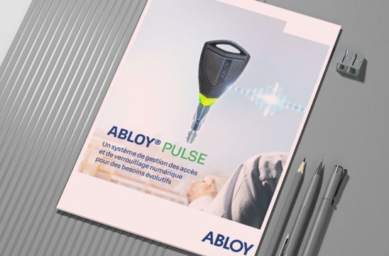 Une brochure ABLOY PULSE, posée sur un bureau à côté de crayons, montre une clé électronique sur sa couverture