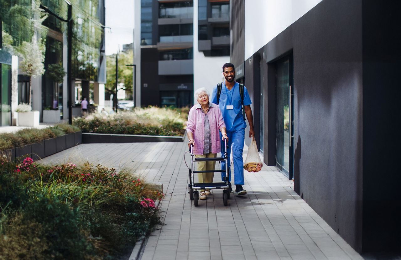 Male  nurse walking home with senior woman after shopping both are smiling