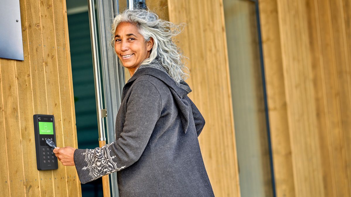 Woman with gey hair uses a key to open a residential entrance door.