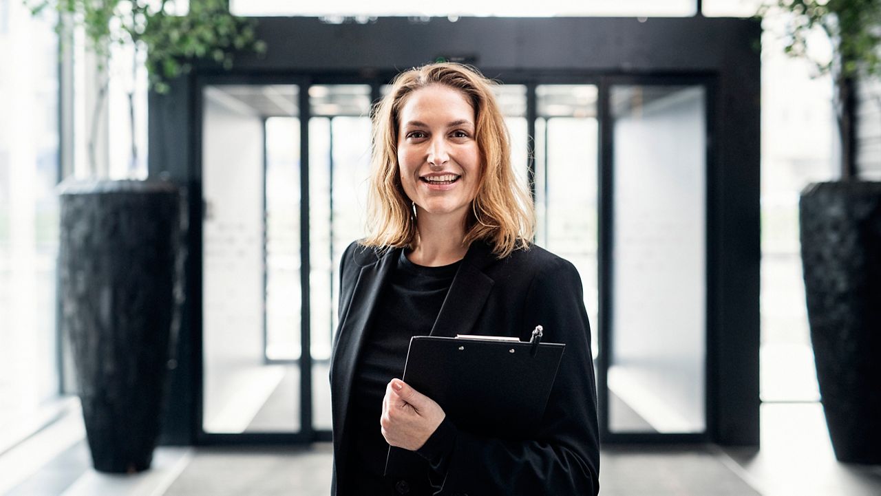 En leende kvinna i svart kavaj som jobbar inom hotellbranschen.