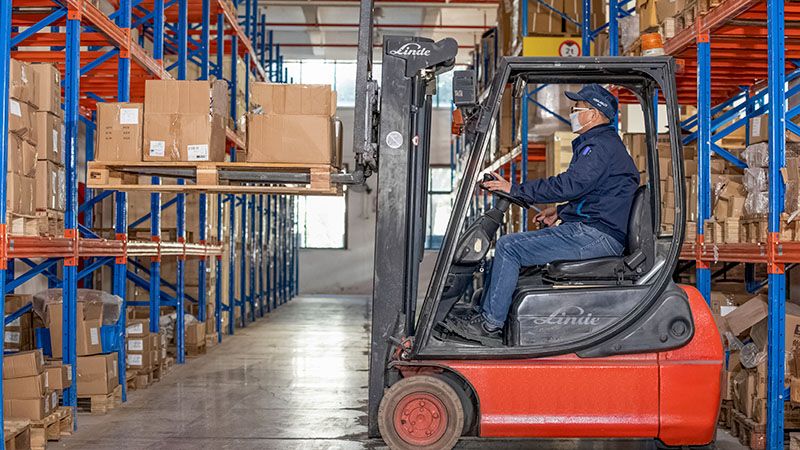 Mann kjører lastebil på et lager.