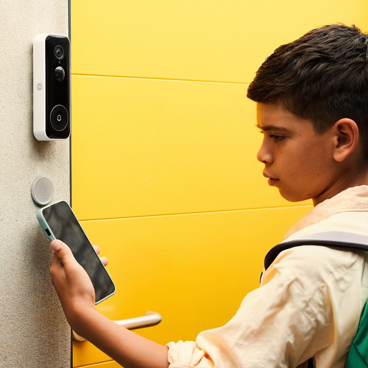 Yale dot on wall outside and boy who opens lock with smartphone.