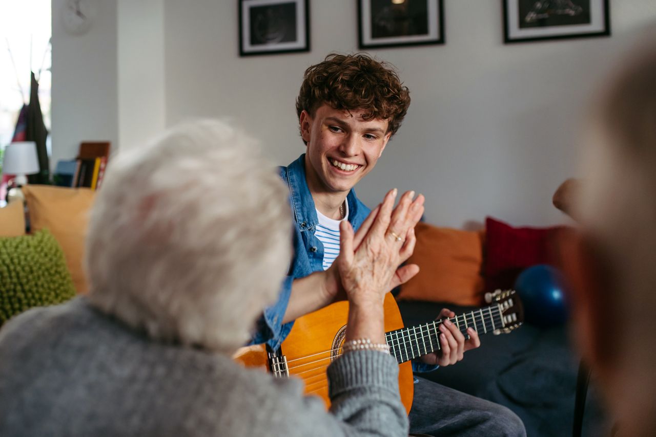 Ung man spelar gitarr för ett par äldre personer.